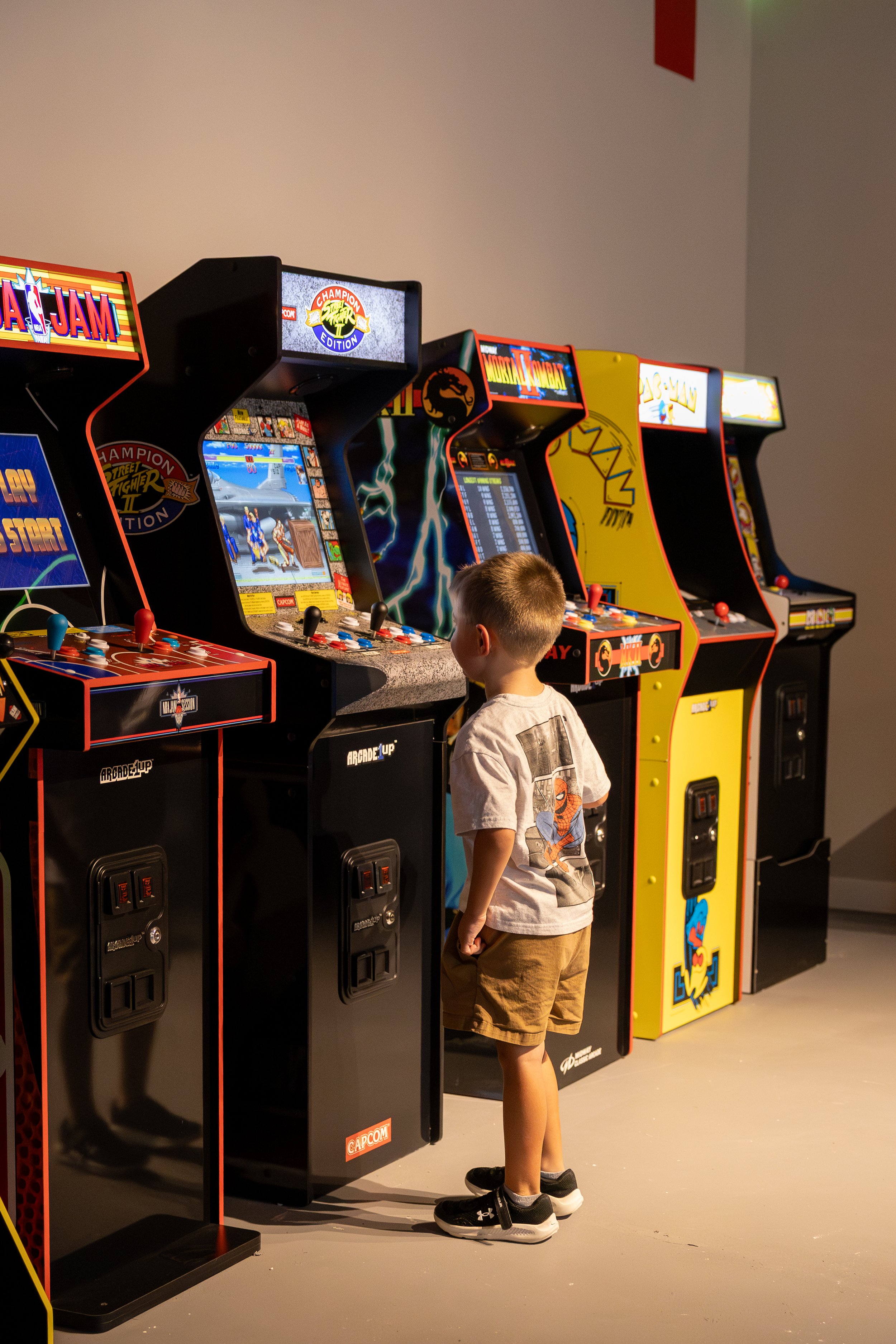 A young boy playing an arcade fighting game in an arcade with multiple arcade machines lined up side by side.