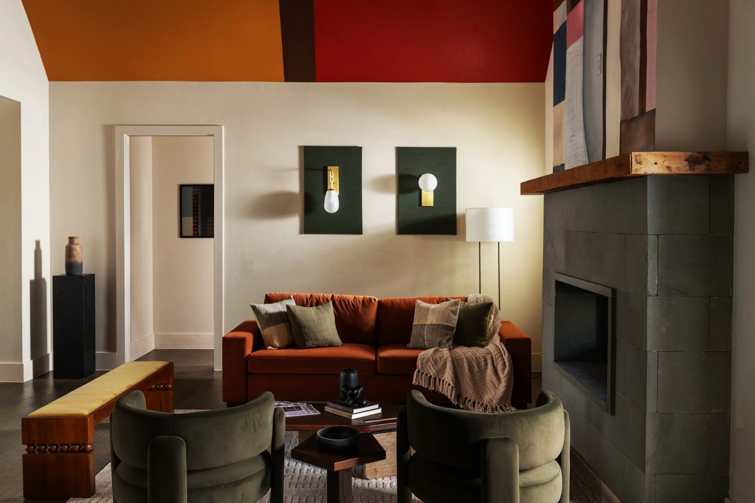Living room with orange sofa, green armchairs, wooden coffee table, fireplace, and modern wall art.